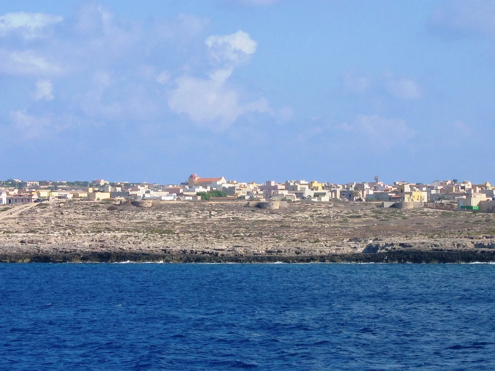 Il paese di Lampedusa visto dal mare sotto un cielo di nuvole bianche
