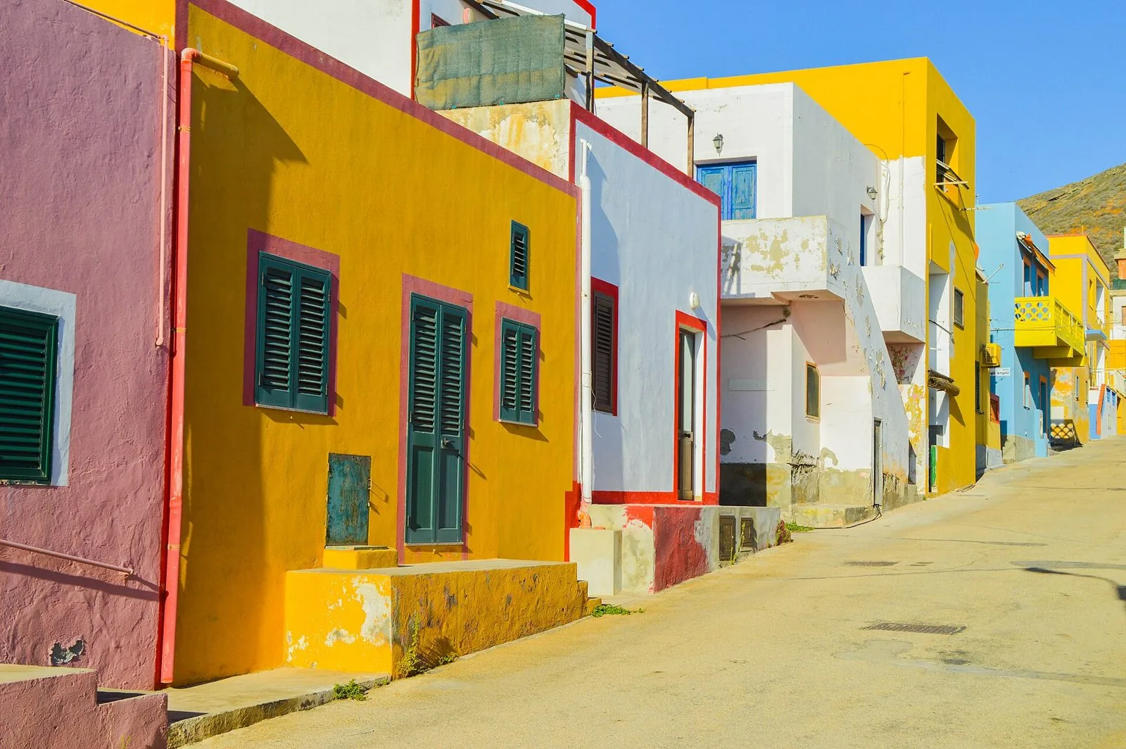 Una strada del paese di Linosa con le case basse dipinte di giallo, rosa, bianco e azzurro sotto il cielo limpido