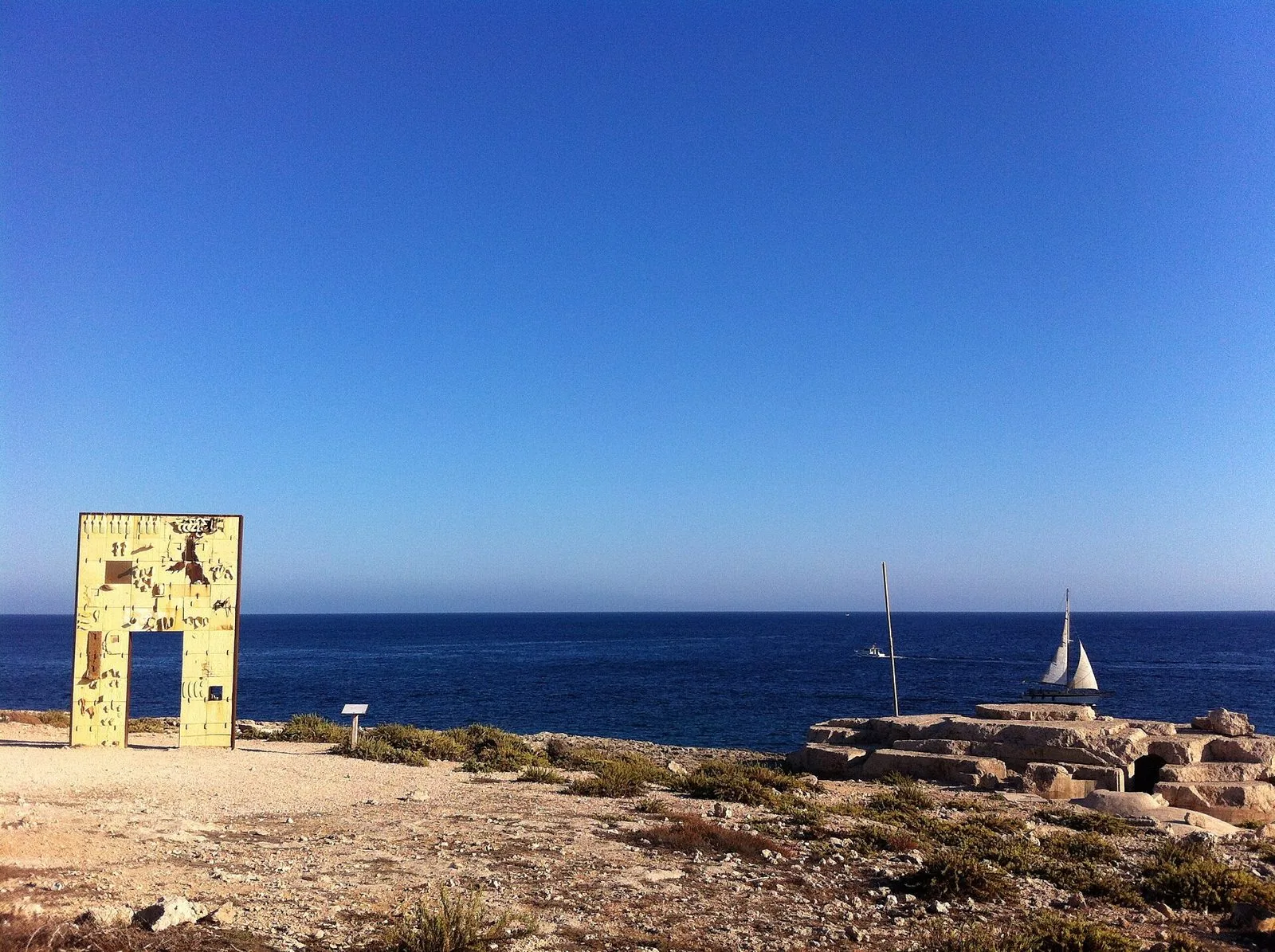 Il monumento Porta di Lampedusa – Porta d'Europa di Mimmo Paladino sulla costa rocciosa, con il mare blu sullo sfondo