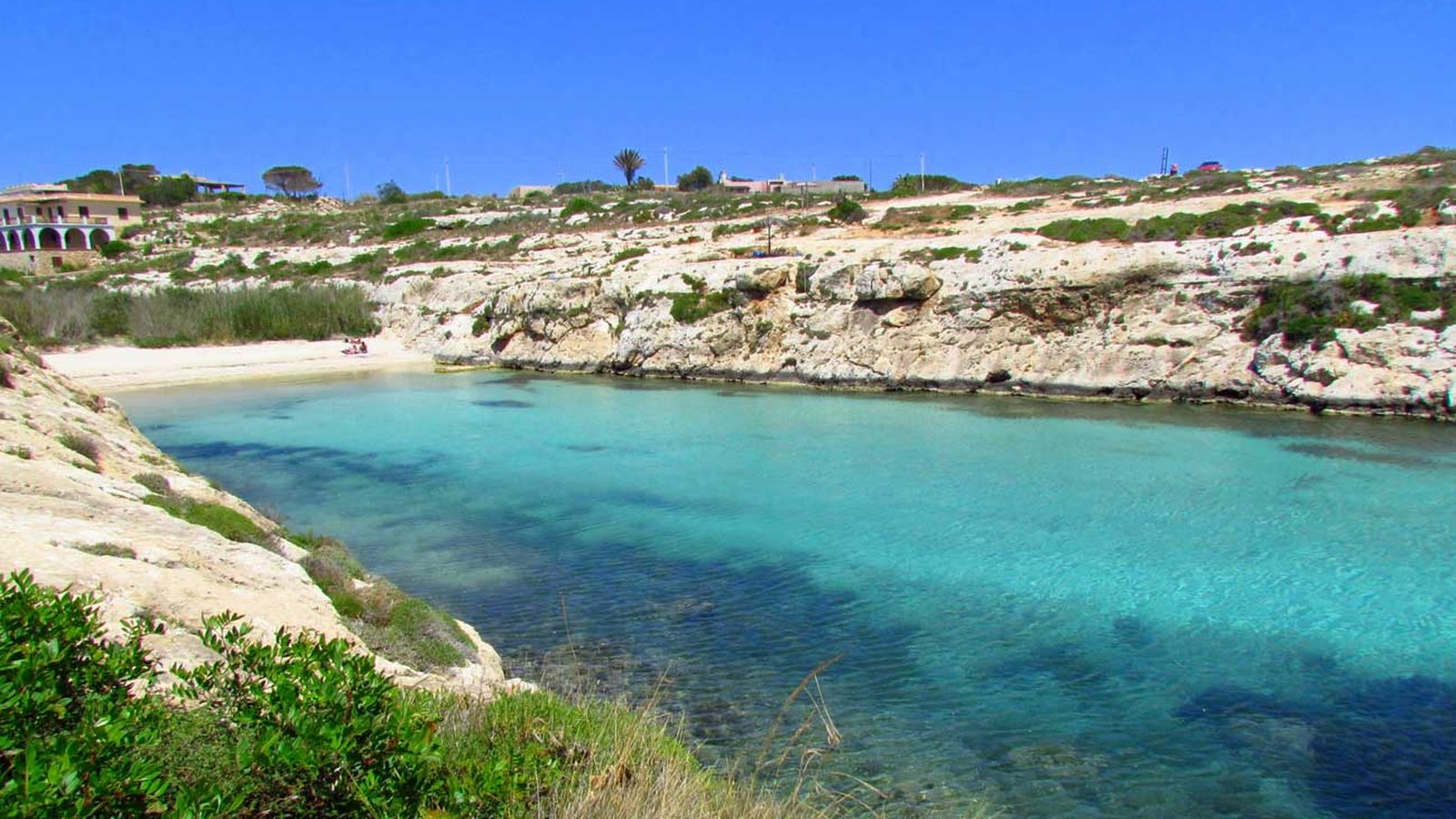 Una cala dall'acqua turchese tra rocce chiare e macchia mediterranea
